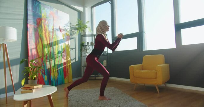 Sporty Muslim young woman training in living sunny room in apartment. Fitness female making lunges at home in modern room. Home fitness concept. Workout, training in quarantine, sport and wellness