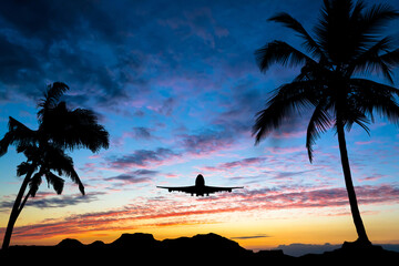 Sunset with silhouettes of mountains and palm trees on the sides of the photo and a flying airplane. Travel concept.