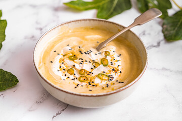 Bright photography of a vegan cream soup on a marble table. Vegetables recipe of a summer cold soup. Puree of seasonal products among fig leaves.