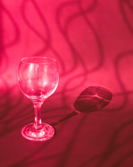 An empty wine glass on a pink background with sunshine shadow effect. The play of light and shadows creates a whimsical picture on the background. 