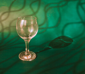 An empty wine glass on a green background with sunshine shadow effect. The play of light and shadows creates a whimsical picture on the background. 