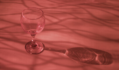 An empty wine glass on a red background with sunshine shadow effect. The play of light and shadows creates a whimsical picture on the background. 