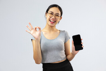 Cheerful asian woman holding a smartphone with black screen and standing on white background