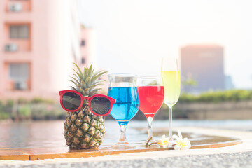Summer funny  pineapple in sunglasses,cocktail drink at edge poolside is decorated by flower.