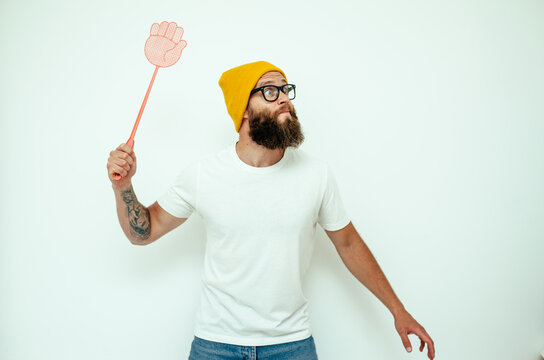 Young caucasian hipster man holding a fly swatter wanting to kill annoying mosquito or a fly.
