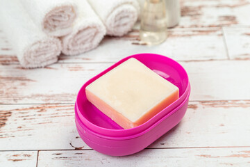 soap on pink plastic soap dish with towels on white wooden table in bathroom
