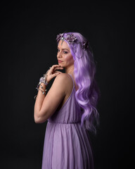 Close up portrait of a purple haired  girl wearing fantasy corset dress with fairy wings and flower crown, casting a spell.  Posing against a dark studio background 