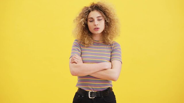 A confident blonde woman is holding hands while listening the viewer standing isolated over yellow wall in the studio