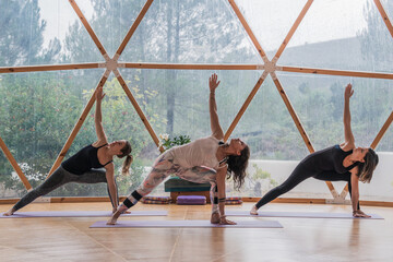 Women stretching up with raised hands in warrior pose on yoga mats in class