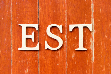 Alphabet letter in word EST  (abbreviation of established, estimated, eastern time zone, expressed sequence tag) on old red color wood plate background
