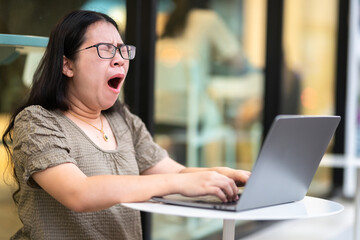 asian of freelance business female bored yawning in front of casual working with laptop computer and coffee and smartphone in coffee shop like the background,covering her mouth out of courtesy
