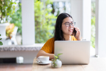 Obraz premium Happy of asian freelance people business female hold pick up smartphone casual working with laptop computer with coffee cup in coffee shop like the background,communication concept