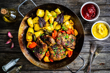 Tasty roasted ribs with baked potatoes and  vegetables served on frying pan on wooden table
