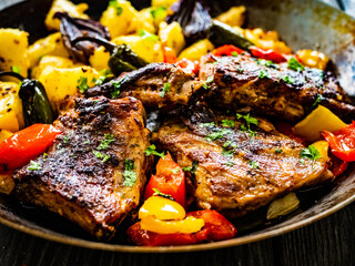 Tasty roasted ribs with baked potatoes and  vegetables served on frying pan on wooden table
