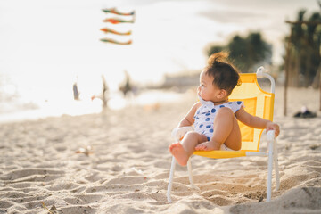 baby in white dress sit on the chair beach yellow color with relaxing and the wind blows in evening...