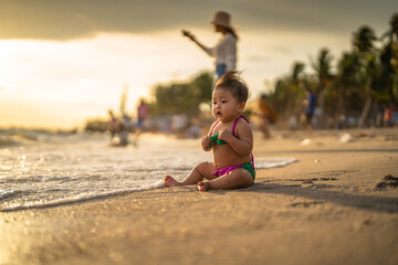 Fototapeta na wymiar baby in bikini sit on the beach with relaxing and the wind blows in evening time and beautiful sunset light at the beach