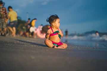 baby in bikini sit on the beach with relaxing and the wind blows in evening time and beautiful sunset light at the beach with blur background people play the sea