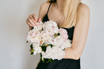 A rich bouquet with peonies in the hands of a girl on a light background. Romantic festive bouquet. Fresh floral. A holiday gift. Beautiful white flowers. The florist girl gathered a bouquet