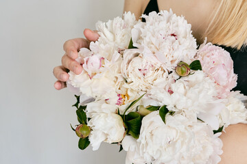 A rich bouquet with peonies in the hands of a girl on a light background. Romantic festive bouquet. Fresh floral. A holiday gift. Beautiful white flowers. The florist girl gathered a bouquet