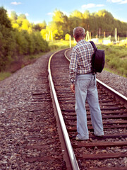 Elderly man in plaid shirt and denim pants with black backpack stands on rails of railway track