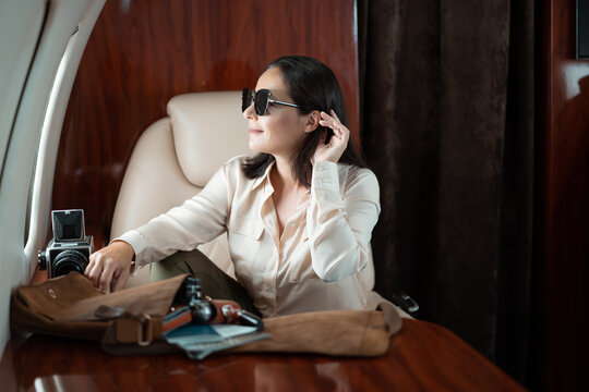 Successful young business woman with sunglasses looks at airplane window during flight in private plane business jet.