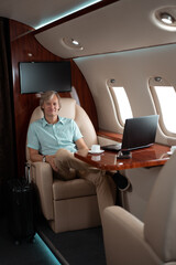 Fototapeta premium Attractive and successful businessman working on a laptop while sitting in the chair of his private jet