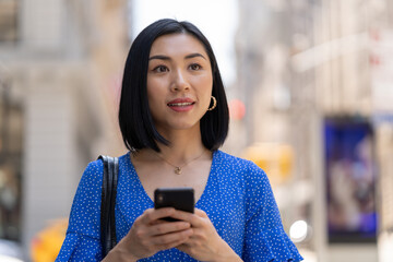 Young Asian woman in city walking using cellphone