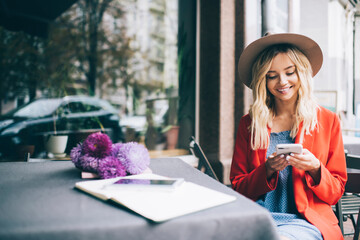 Happy Caucaisan customer resting at street terrace using smartphone technology for writing web...