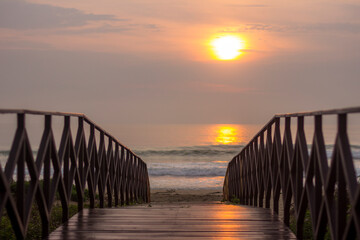 Fototapeta na wymiar Landscape. Deck Bridge over the sand at the beach with the on background at the sunrise