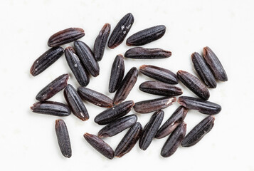 several raw black rice grains close up on gray