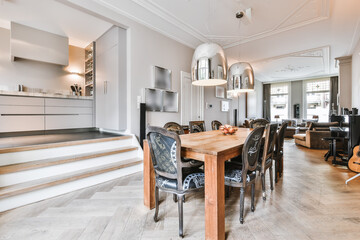 Elegant chairs around wooden dining table under pendant lamps in modern apartment with ornamental...