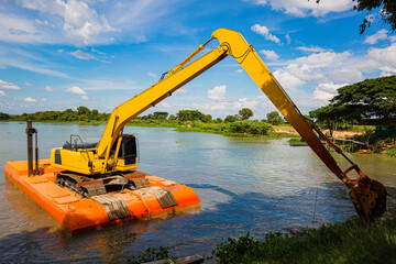 The yellow backhoe is working at the river floatin