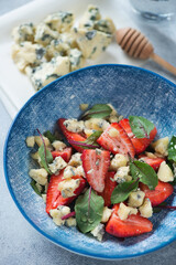 Close-up of salad with fresh strawberry, mangold leaves and gorgonzola cheese served in a blue bowl, vertical shot