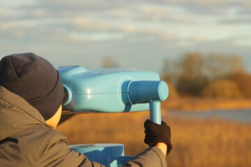 A boy looks through panoramic binoculars on a viewing platform in autumn fall national park