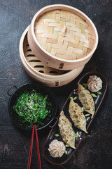 Panasian steamed dumplings with seaweed salad over dark brown stone background, high angle view, vertical shot