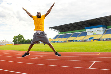 Obraz premium Full length photo of handsome afro american black sportsman jump high up wear shorts, sneakers and yellow t-shirt at the stadium, doing morning exercises or celebrating victory, goal, successful match