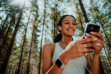 Mixed race female teenager exercising in forest texting on cellular device 