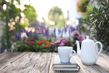 White coffee cup and teapot and notebooks on wooden table with flowers in the back