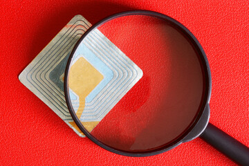 RFID tag transponder under magnifying glass. A concept for the use of wireless RFID technology in...
