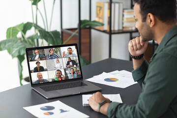 Fototapeta na wymiar Meeting online concept. Young indian man using laptop for video calling with colleagues, employees in office, online meeting with many people together