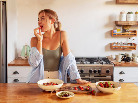Young woman prepares oatmeal for breakfast with strawberries in the kitchen.