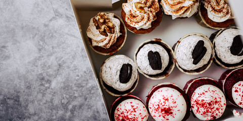 Variety of delicious cupcakes presented in a white box with copy space. Red Velvet cupcake, dark cookie and carrot cupcake with walnuts and cream.