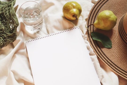 Trendy summer mockup. Green cotton bag, water glass, pears, album blank sheet and straw hat. Flat lay travel aesthetics photography