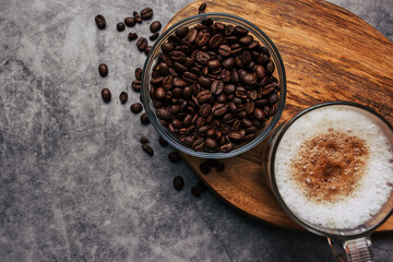 Coffee beans in a transparent bowl over a wood tablet with copy space. Dark background of coffee beans.
