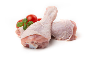 Raw chicken legs with skin decorated with tomatoes and basil on a white background.