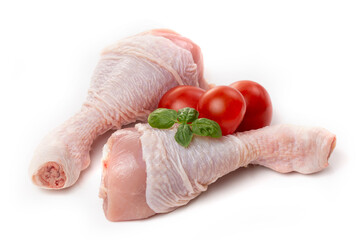Raw chicken legs with skin decorated with tomatoes and basil on a white background.