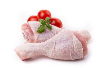 Raw chicken legs with skin decorated with tomatoes and basil on a white background.