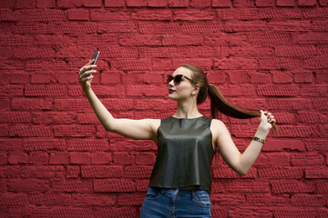 Millennial female blogger shooting influence vlog via cellphone front camera using mobile application at publicity area with copy space area, Caucasian hipster girl in sunglasses taking selfie photos