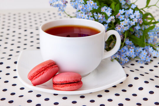 A cup of tea and tender strawberry macarons with a bouquet of wild forget-me-nots
