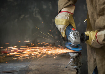 a man with the help of an angle grinder saws a welding seam on the metal clamped in a vice